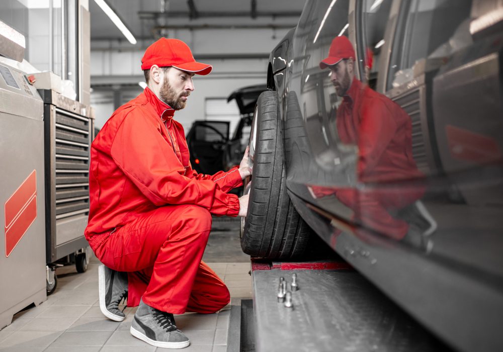 Two car service workers in red uniform changing wheel of a sport car at the tire mounting service